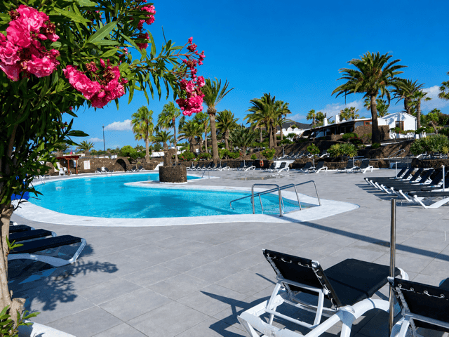 Swimming pool at Casa del Sol with sun loungers, palm trees and tropical gardens under a blue sky.