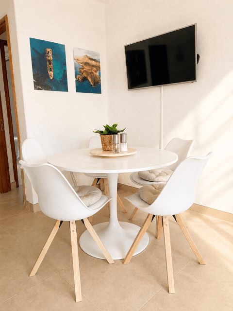 Dining room in Casa del Sol with round table, white chairs and television on the wall.